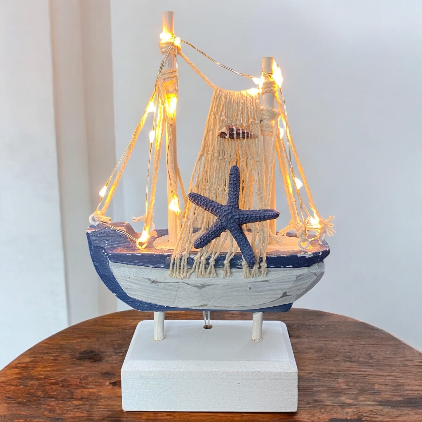 Maritimes Deko Segelboot aus Holz mit LED-Beleuchtung, Netz, Seestern und Fisch in Weiß, Dunkelblau und Creme im Ambiente