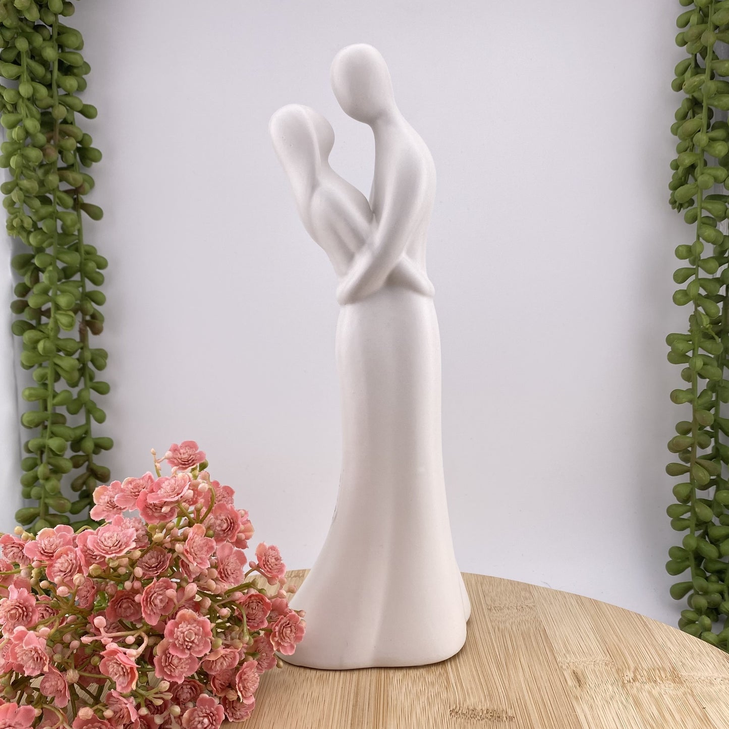 Eine weiße Dekofigur in Form eines verliebten Paares. Das Ehepaar hält sich gegenseitig im Arm und ist im Ambiente platziert.