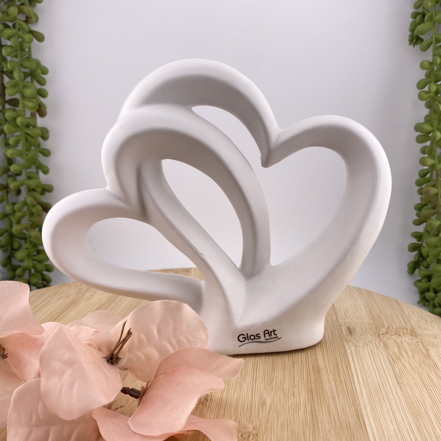 Eine weiße Dekofigur in Form zweier Herzen mit Aussparungen, die ineinander übergehen. im Ambiente platziert.