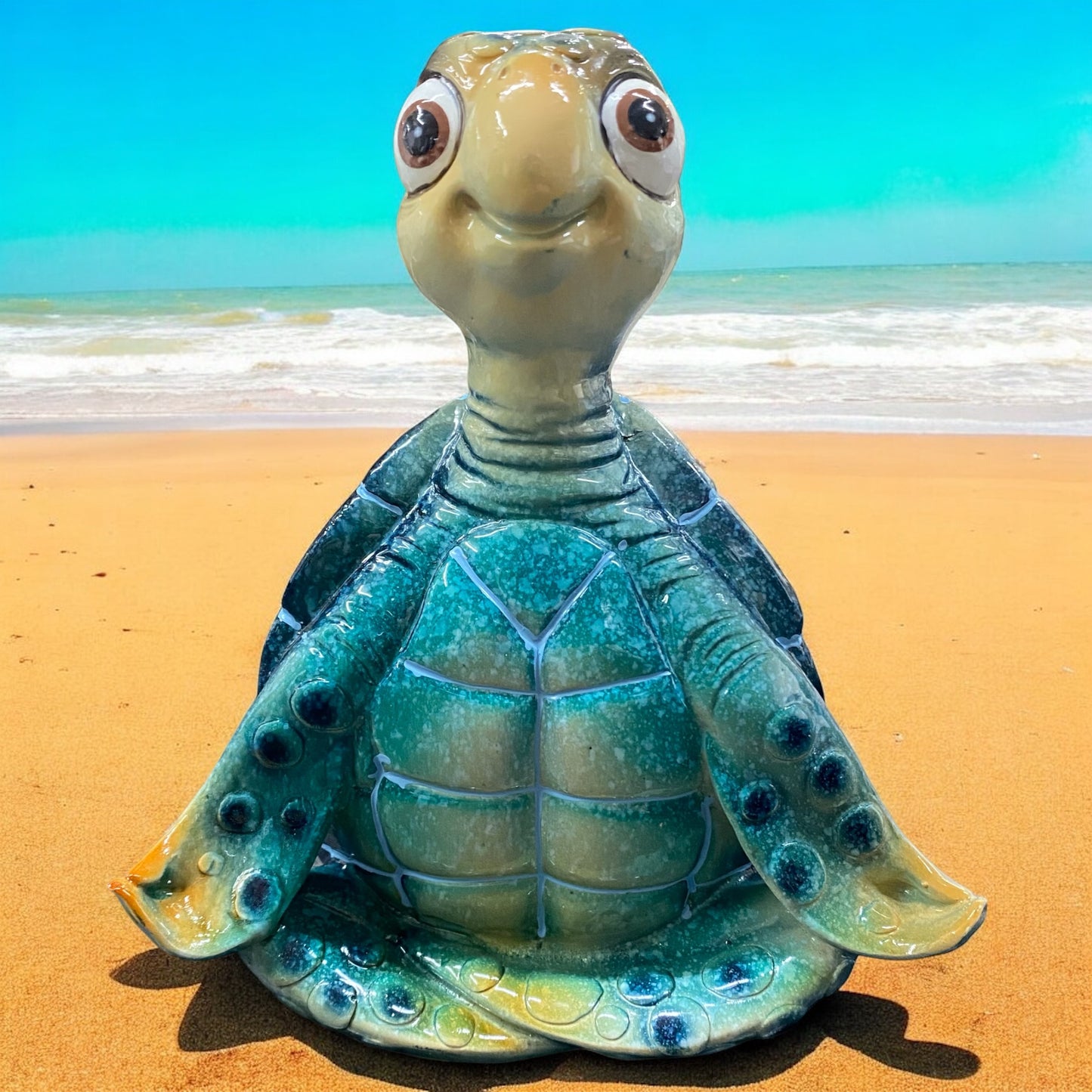Eine blaue Schildkröte Dekofigur sitzt meditierend vor weißem Hintergrund platziert. Ihre braunen Augen sind geöffnet und sie lächeln zufrieden.