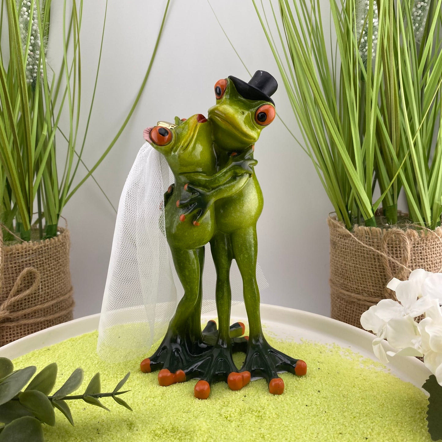 Eine Dekofigur im Ambiente, die ein Frosch Brautpaar bei der Hochzeit abbildet. Die Froschdame trägt einen Schleier und der Froschbräutigamm einen Hut.