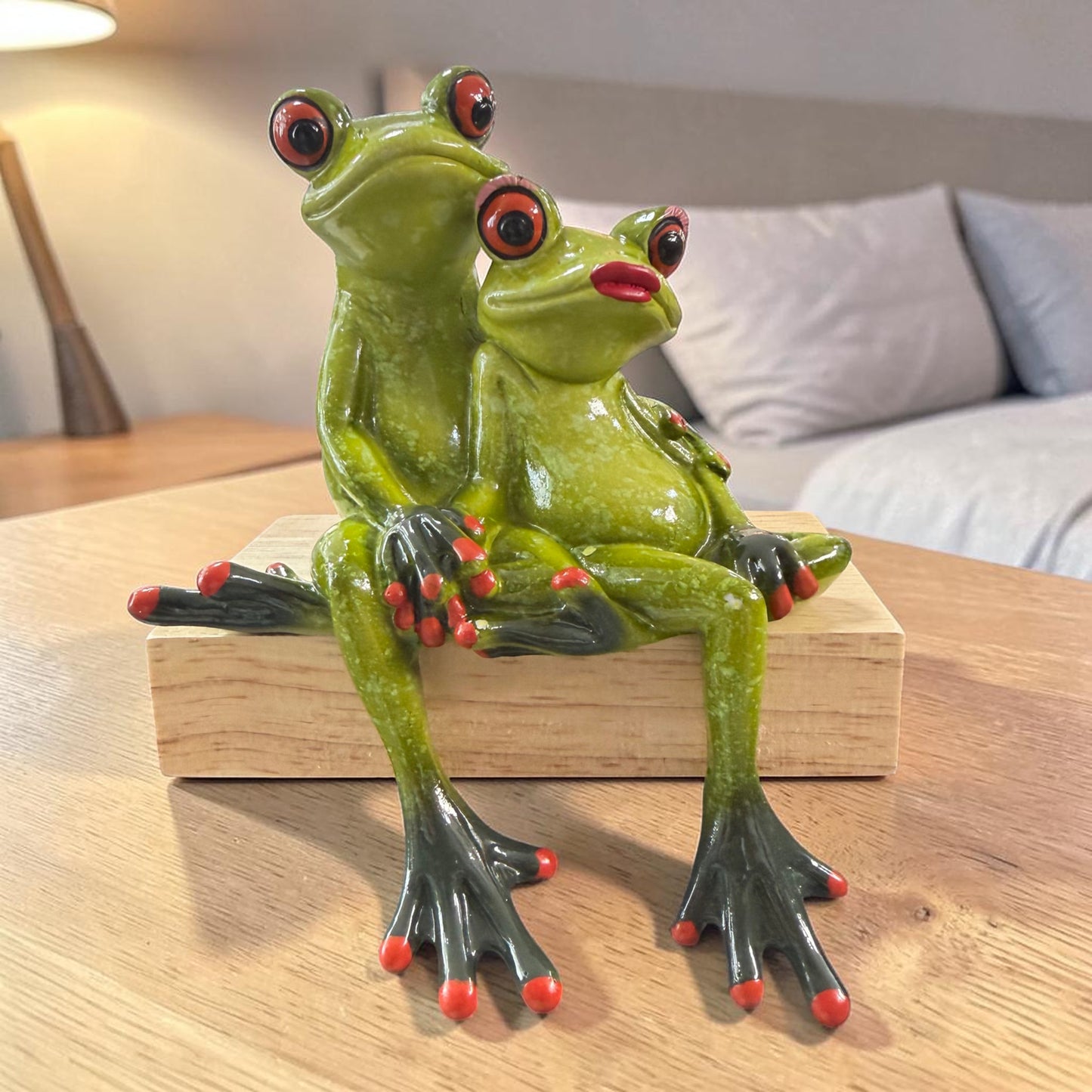Zwei grüne Formano Frösche sitzen hintereinander auf einem hellen Holzsockel vor weißem Hintergrund.