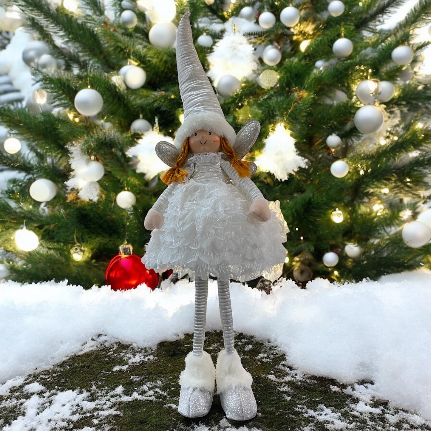 Eine stehende Stoff-Engelfigur mit langen Beinen, Zipfelmützen und flauschigem Kleid in Weiß im Ambiente