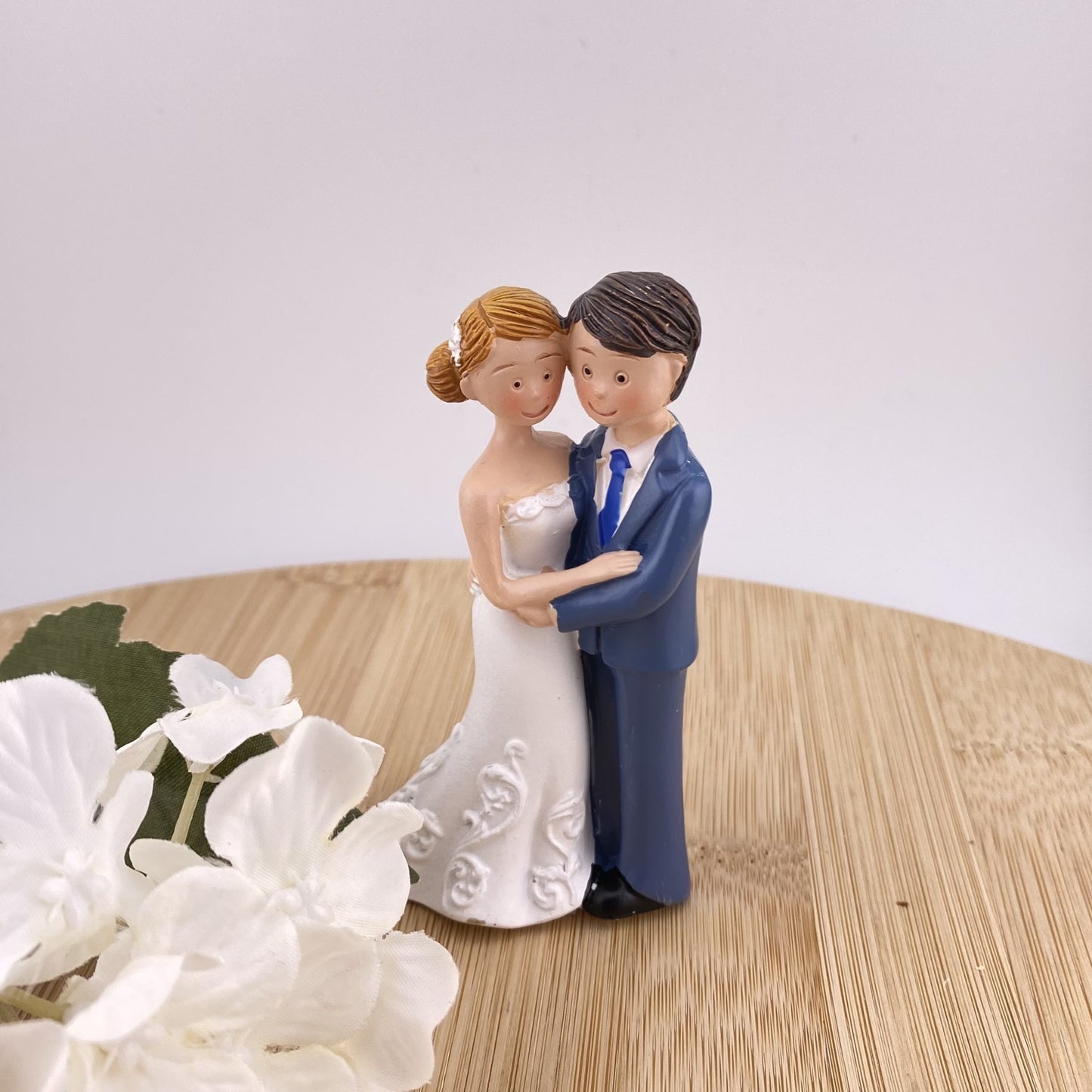 Dekofigur Aufsteller im Ambiente bildet Brautpaar in Brautkleid und Anzug ab, die sich nebeneinander stehend in den Armen liegen.
