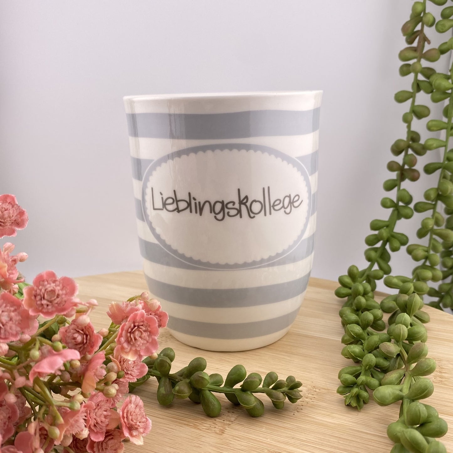 Eine grau weiß gestreifte Kaffeetasse mit Henkel und Schriftzug Lieblingskollege im Ambiente