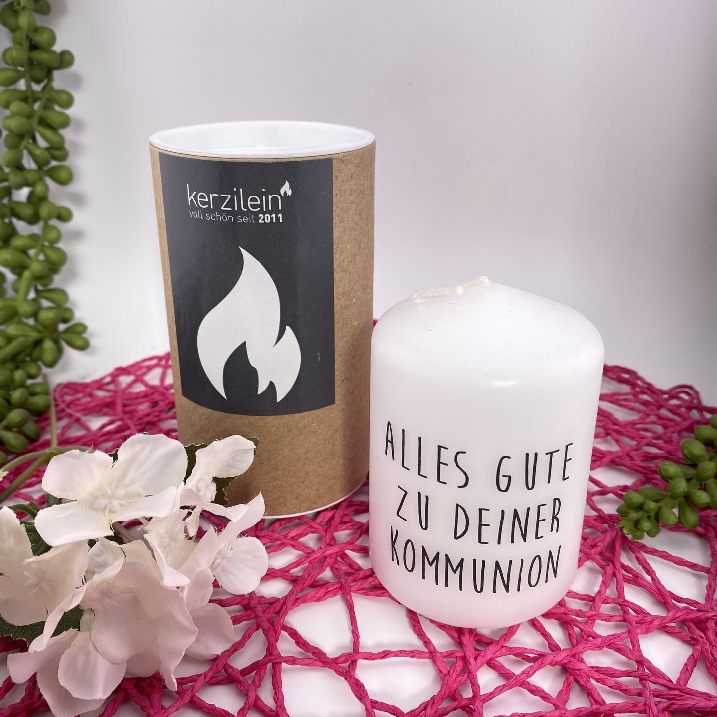 Eine kleine, weiße Kerze mit schwarzem Schriftzug "Alles Gute zur Kommunion". Die Dekokerze ist 8cm groß und im Ambiente platziert.