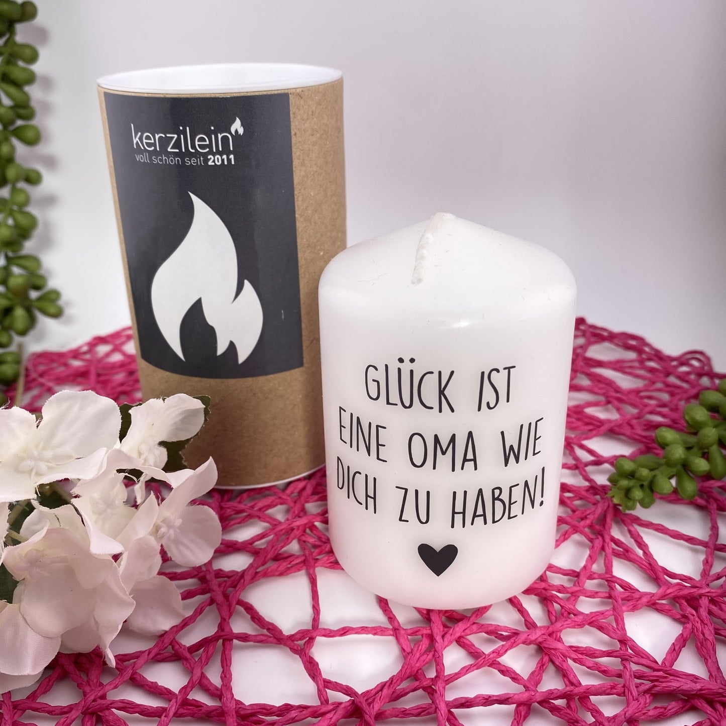 Eine kleine, weiße Kerze mit schwarzem Schriftzug "Glück ist eine Oma wie dich zu haben". Die Dekokerze ist 8cm groß und im Ambiente platziert.