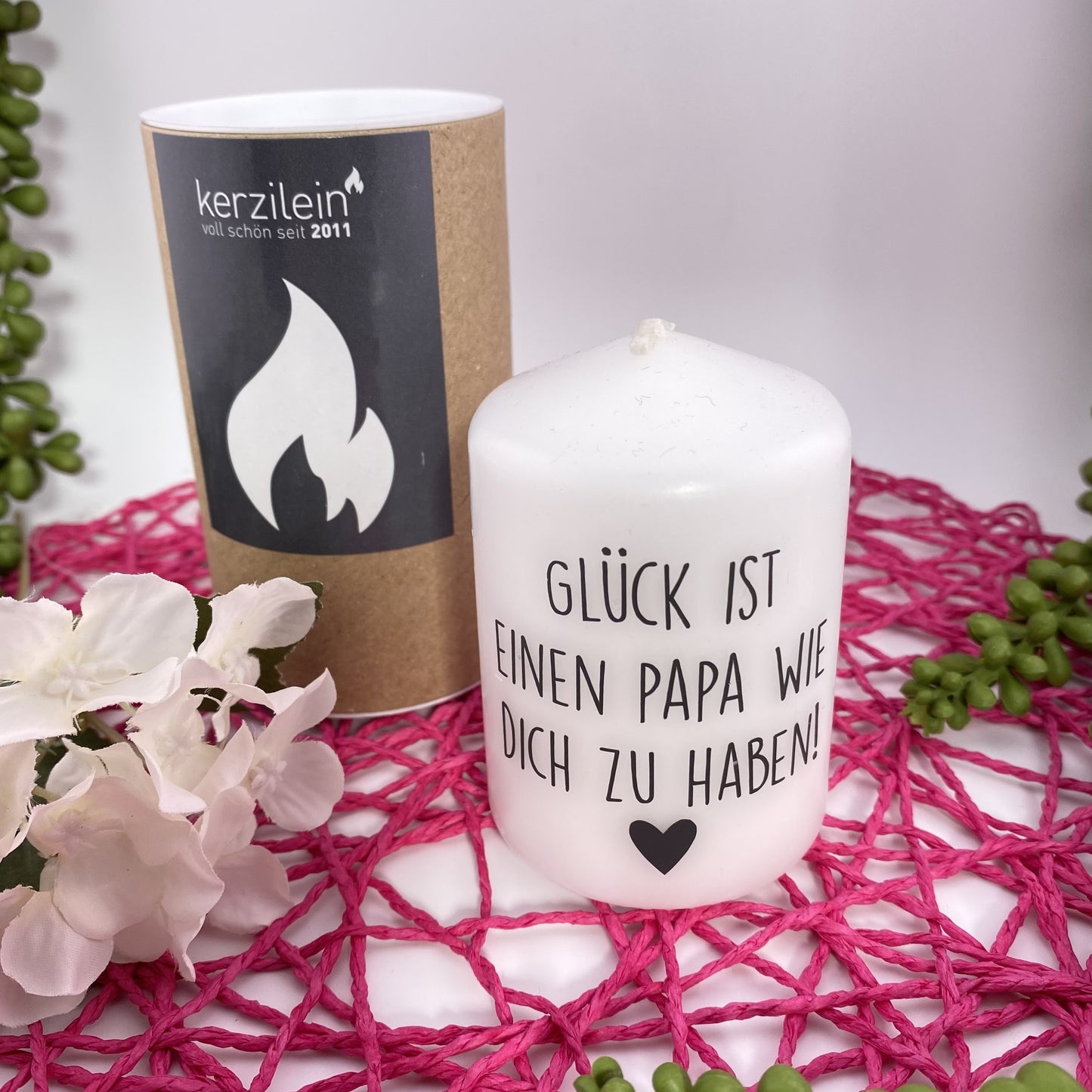Eine kleine, weiße Kerze mit schwarzem Schriftzug "Glück ist ein Papa wie dich zu haben". Die Dekokerze ist 8cm groß und im Ambiente platziert.