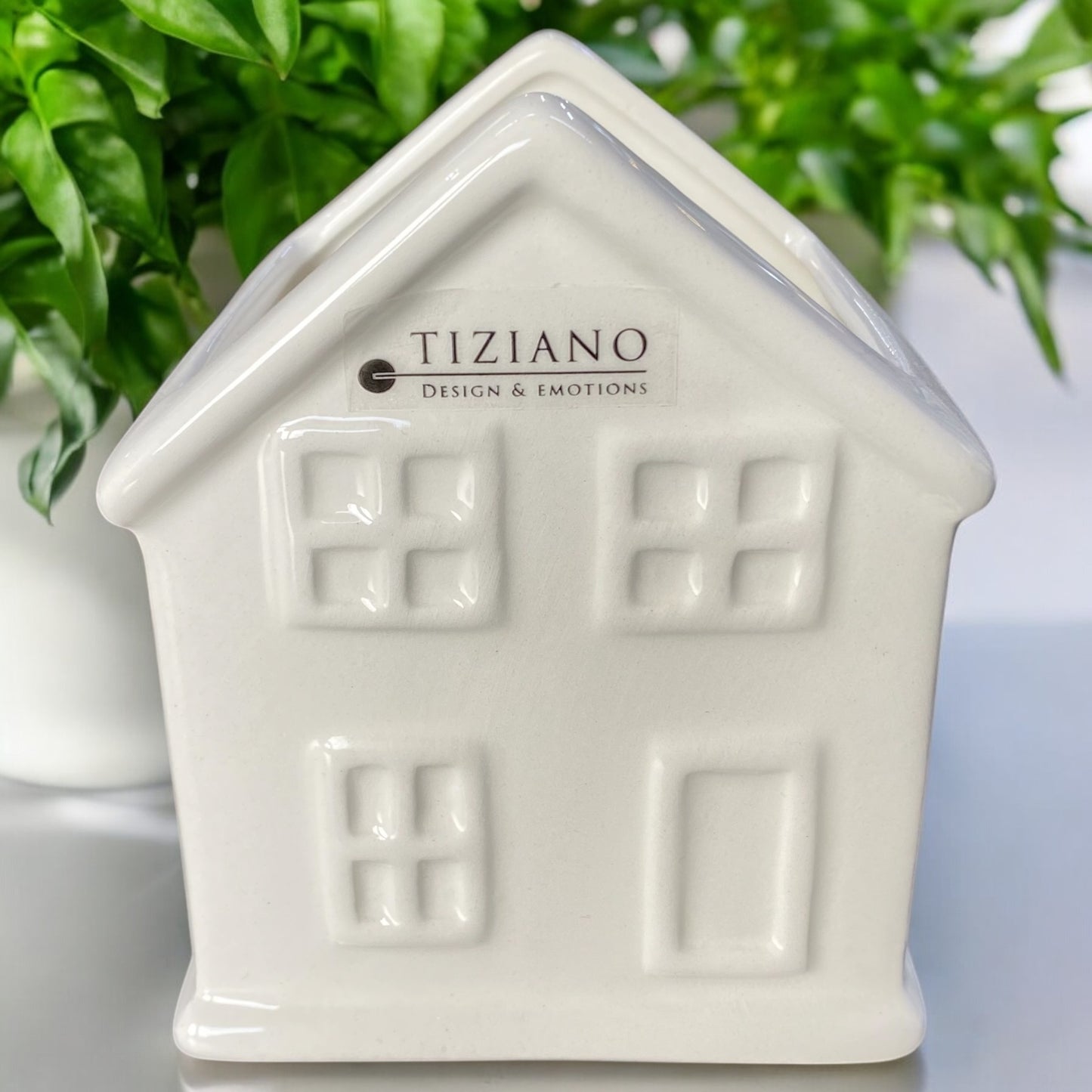 Ein creme-weiße Keramikhaus der Marke Tiziano aus der Serie Skade mit Fenstern und Tür als Pflanzschale im Ambiente.