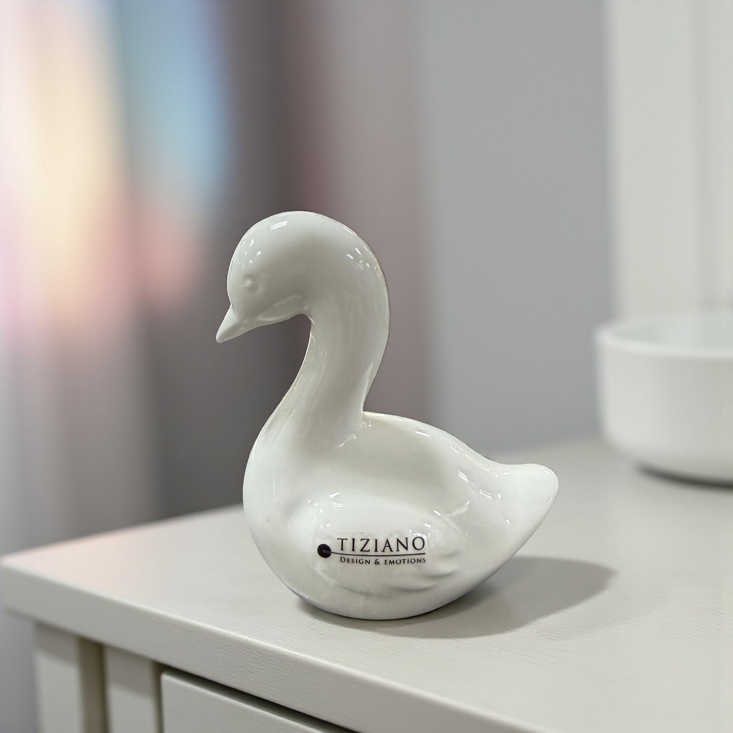Mittlere weiße Keramikfigur in Gansform steht auf einem hellen Möbelstück im Innenraum.