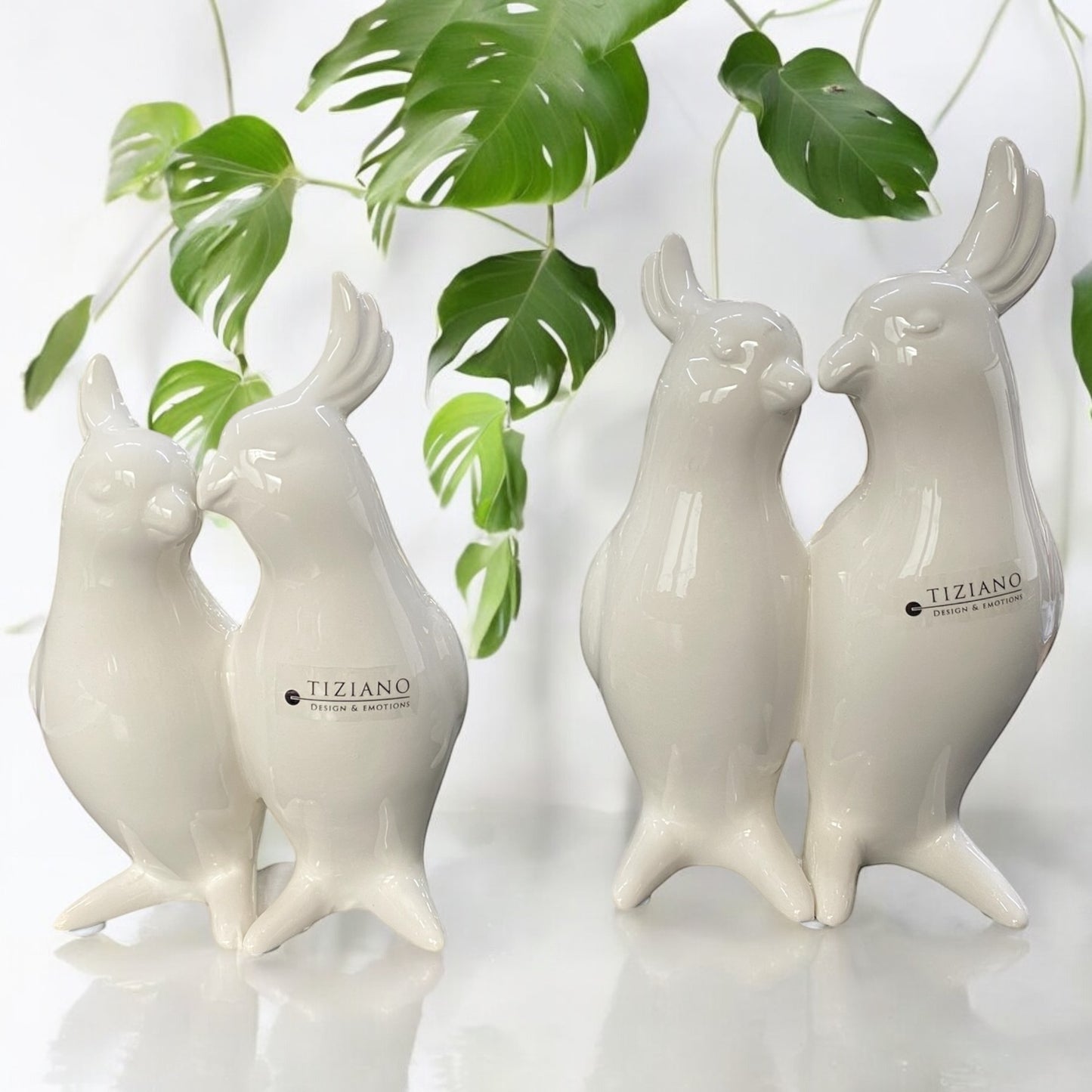 Zwei crème-weiße Keramikfiguren in Form eines Papageienpaars, eng beieinanderstehend mit liebevollem Ausdruck, in zwei Größen nebeneinander im Ambiente dargestellt.