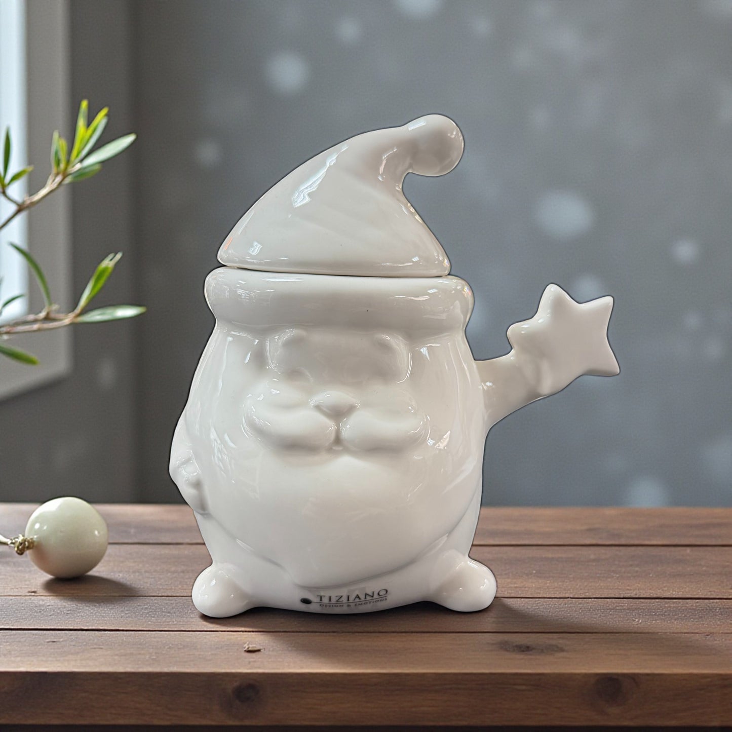 Eine geschlossene weiße Keramik-Gebäckdose in Weihnachtsmannform steht auf einem Holztisch, eine Hand hält einen sternförmigen Arm seitlich hoch.