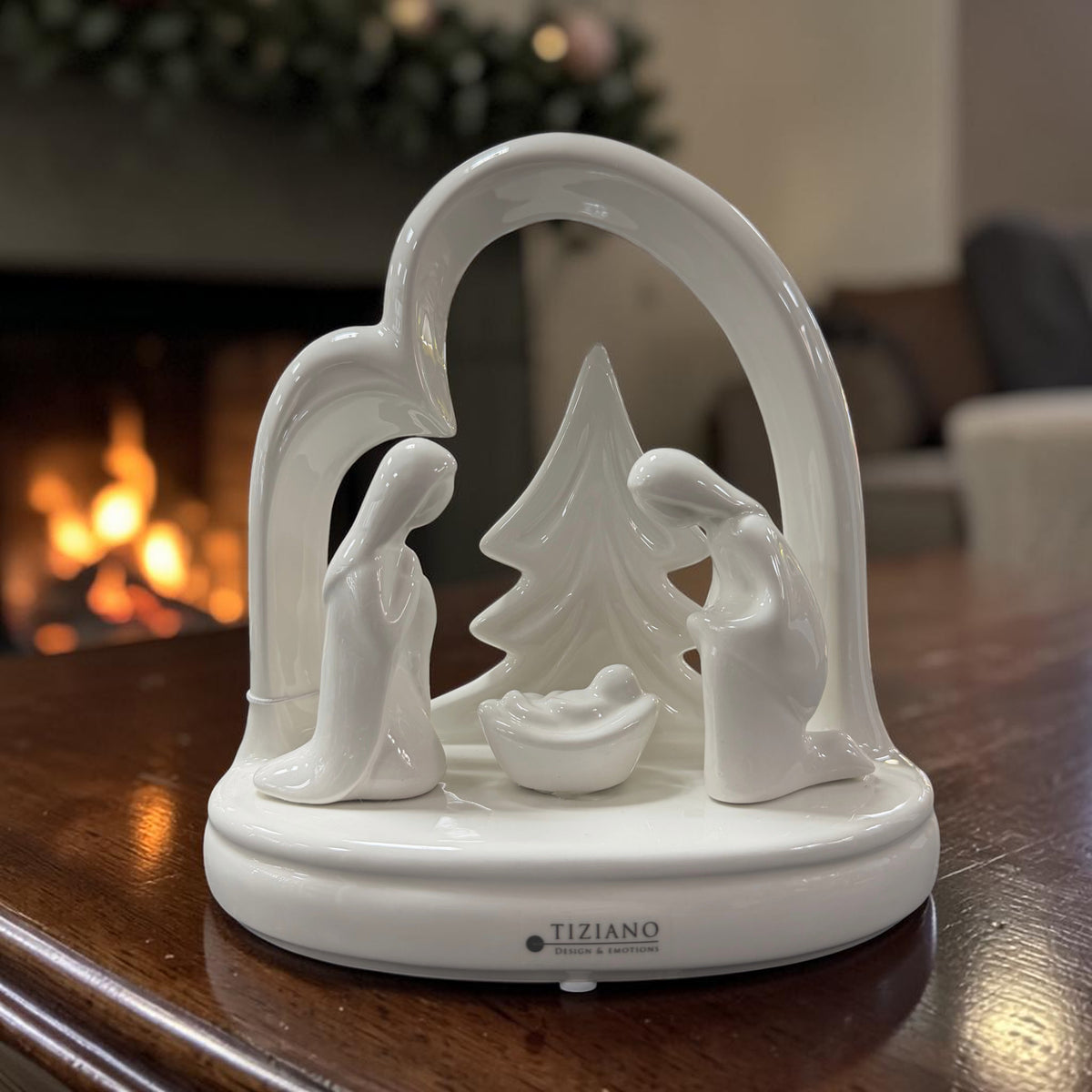Cremeweiße Tiziano Keramik Krippe mit Maria, Josef und Jesuskind vor einem Tannenbaum in herzförmigem Rahmen auf einem Holztisch.