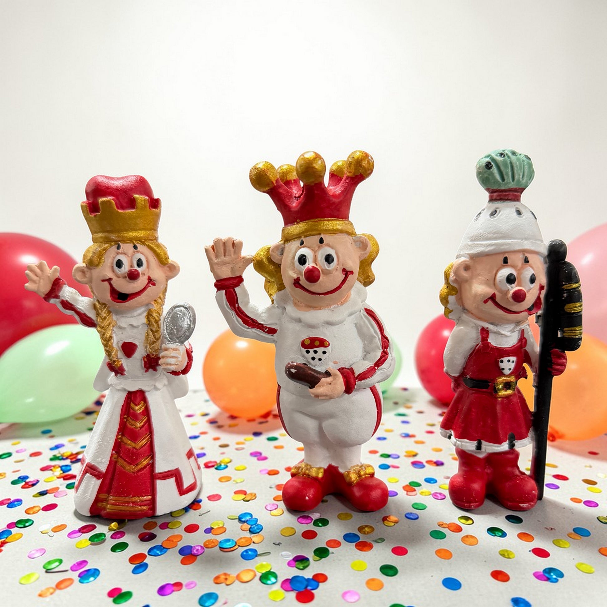 Clown-Dekofiguren als Karnevals-Dreigestirn Bauer, Prinz und Jungfrau vor Luftballons und Konfetti.