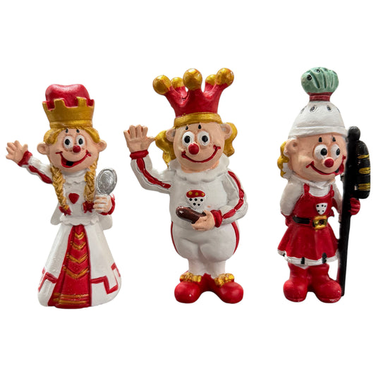 Clown-Dekofiguren als Karnevals-Dreigestirn Bauer, Prinz und Jungfrau auf weißem Hintergrund.