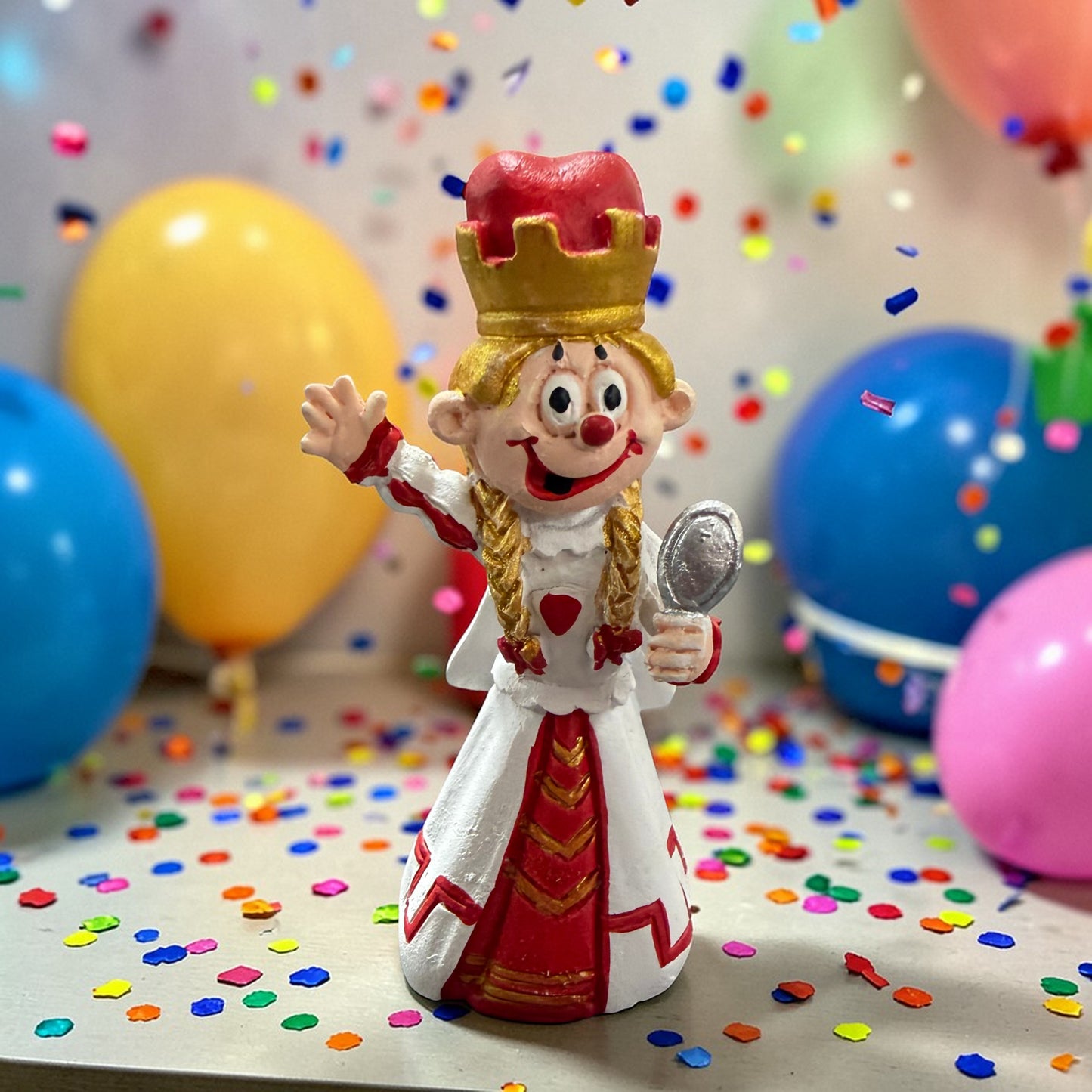 Clown-Dekofigur Jungfrau mit Krone und Spiegel vor Luftballons und Konfetti.