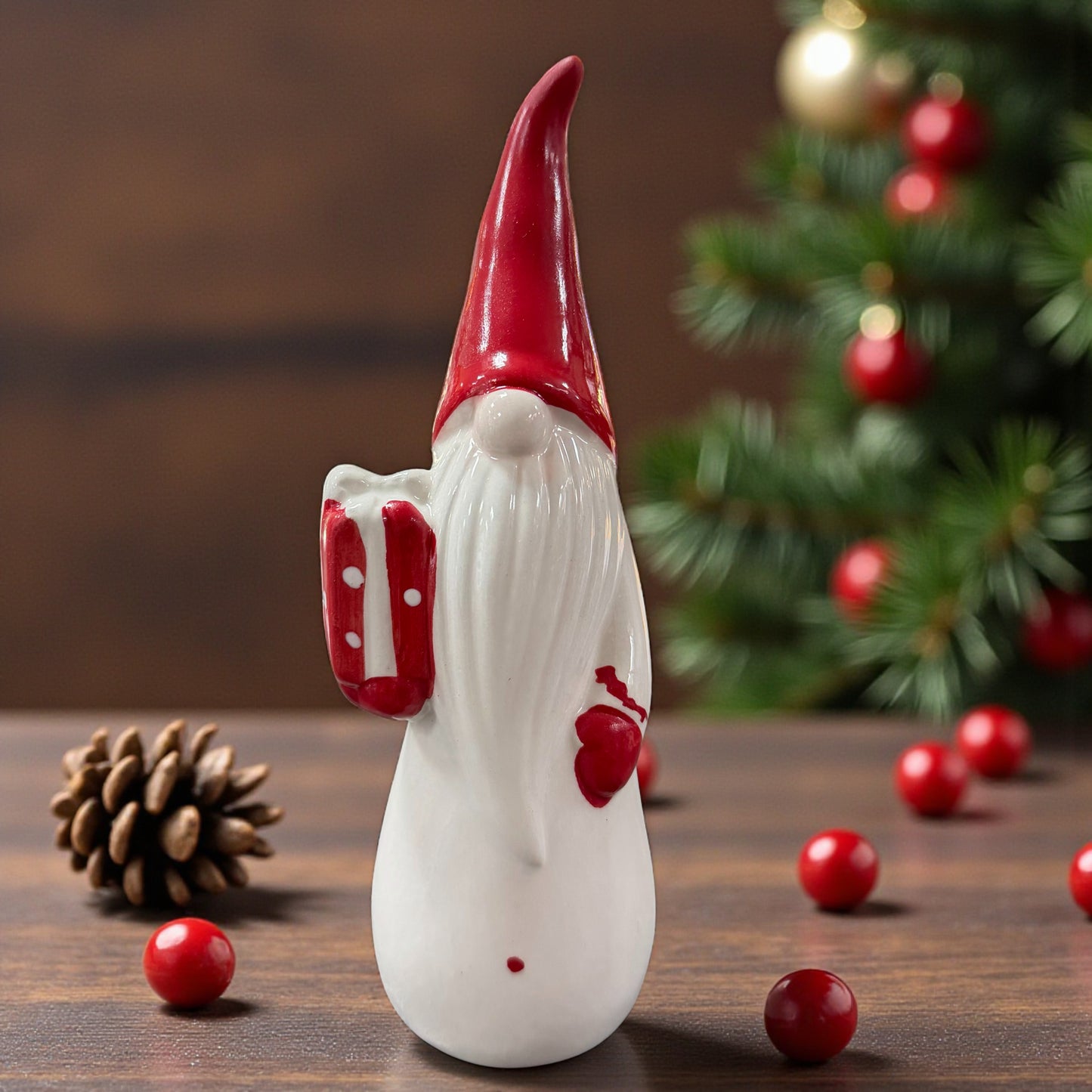 Ein Keramik-Wichtel mit roter Mütze hält ein Geschenk in der Hand und ist stimmungsvoll vor einem Weihnachtsbaum arrangiert.