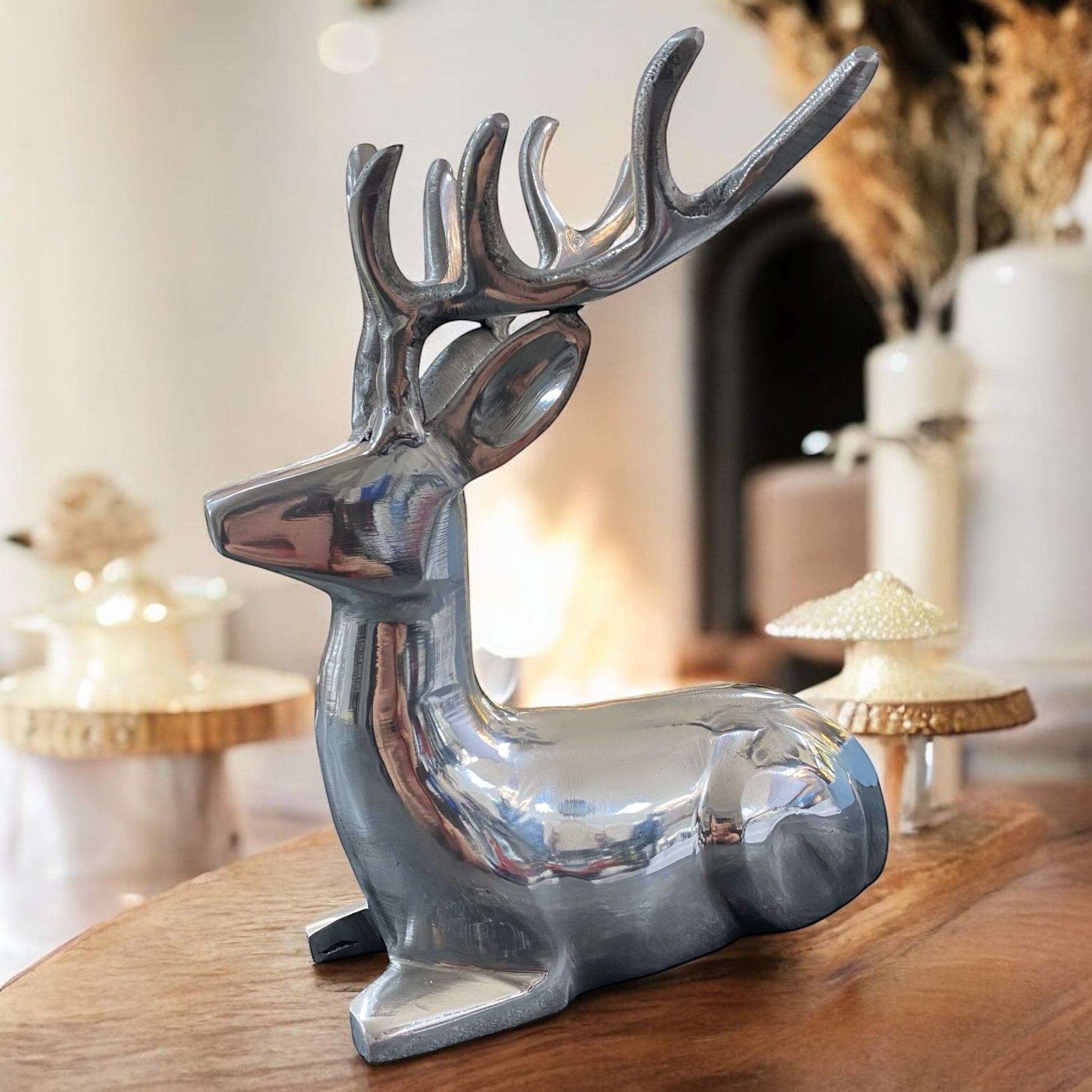 Silberner liegender Hirsch als stilvolle Dekoration auf Holztisch, elegantes Wohnambiente im Hintergrund.
