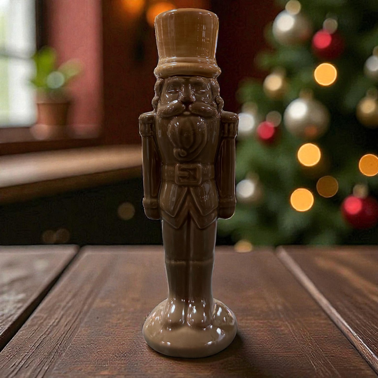 Eine stehende Nussknacker-Figur aus Keramik in dunklem Braun steht auf einer Holzoberfläche vor einem dekorierten Hintergrund.