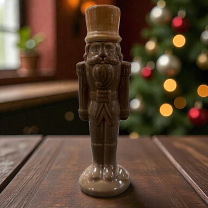 Eine stehende Nussknacker-Figur aus Keramik in dunklem Braun steht auf einer Holzoberfläche vor einem dekorierten Hintergrund.