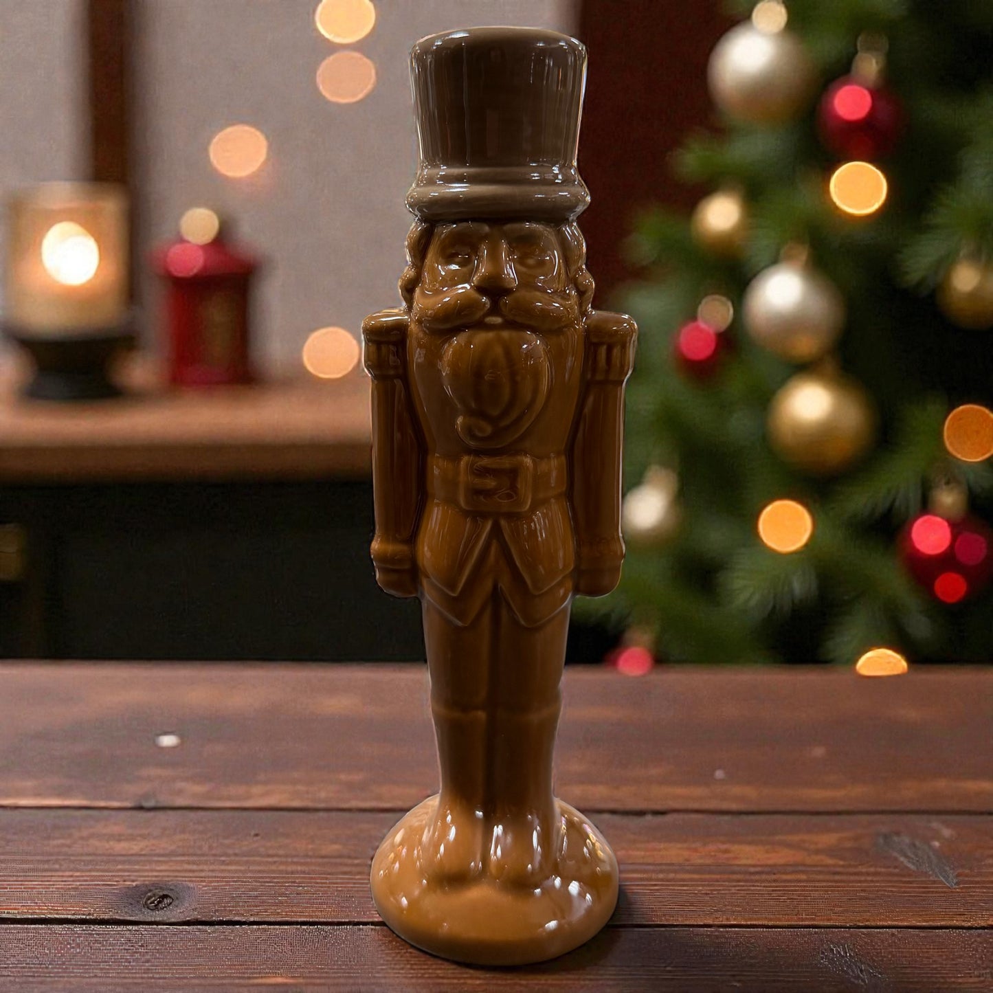 Eine stehende Nussknacker-Figur aus Keramik in hellem Braun steht auf einer Holzoberfläche vor einem dekorierten Hintergrund.