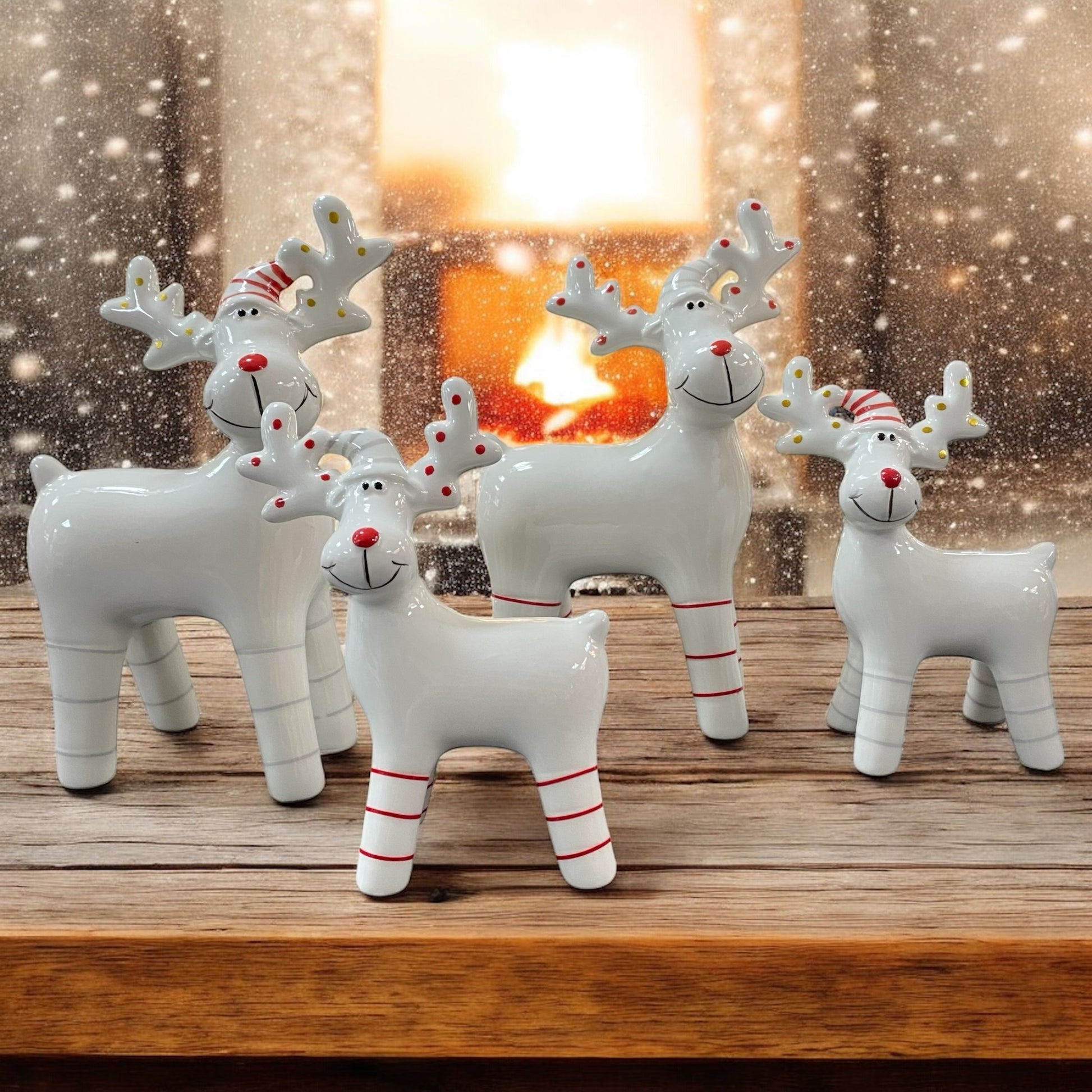 Weihnachtliche Porzellan-Rentiere in Weiß mit roten und goldenen Details, dekorativ vor Kaminfeuer und Schneeflocken arrangiert.
