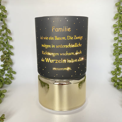 Eine schwarze LED Säule mit goldenem Sockel. Auf dem Dekolicht ist der Spruch "Familie ist wie ein Baum. Die Zweige mögen in unterschiedliche Richtungen wachsen, doch die Wurzeln halten alles zusammen" zu sehen. Das Licht ist 15cm groß und im Ambiente platziert.