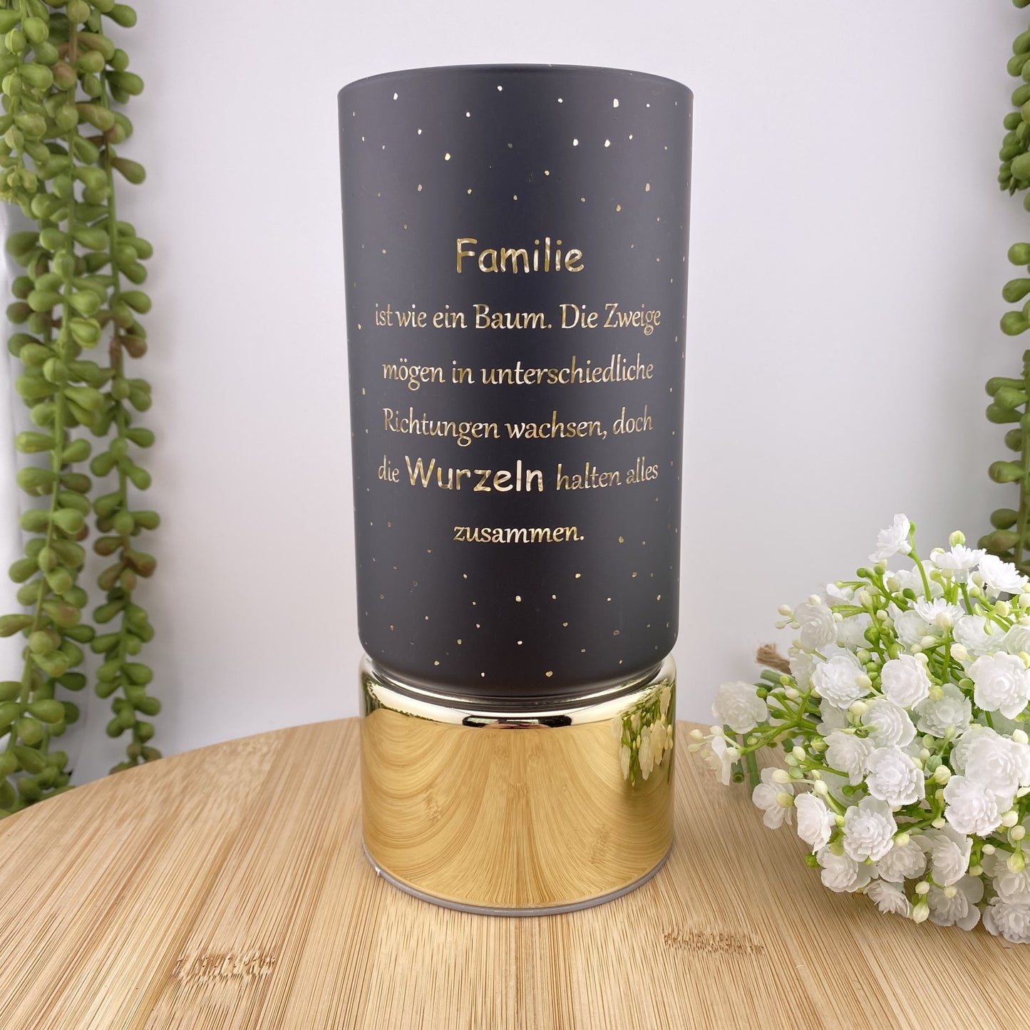 Eine schwarze LED Säule mit goldenem Sockel. Auf dem Dekolicht ist der Spruch "Familie ist wie ein Baum. Die Zweige mögen in unterschiedliche Richtungen wachsen, doch die Wurzeln halten alles zusammen" zu sehen. Das Licht ist 20cm groß und im Ambiente platziert.