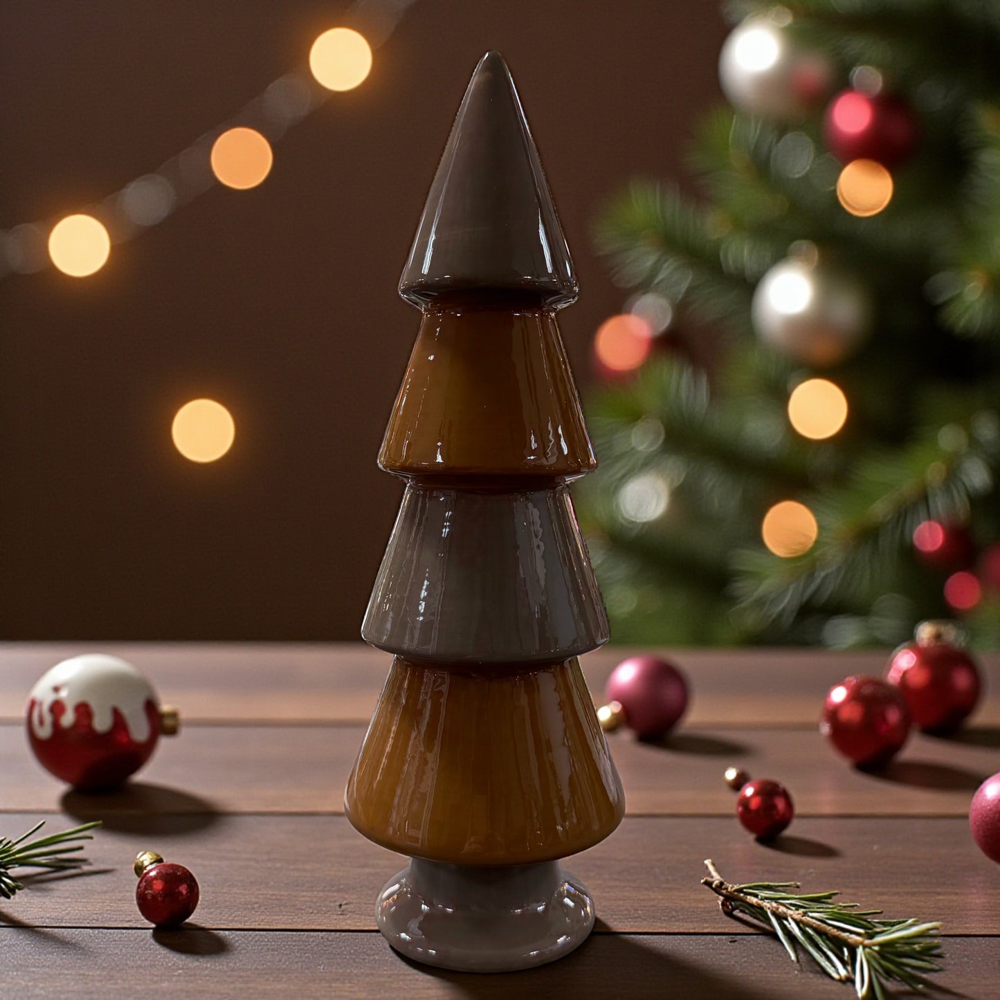 Ein glänzender Keramik-Tannenbaum in Braun steht auf einem Holztisch vor einem weihnachtlich dekorierten Raum mit Tannenzweigen und Kugeln.