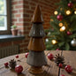 Ein glänzender Keramik-Tannenbaum in Braun steht auf einem Holztisch, umgeben von Weihnachtskugeln und warmen Lichtern im Hintergrund.