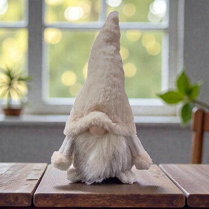 Stofffigur in Form eines Wichtels mit langem spitzem Hut, rundem Nasenbereich und langem Bart steht auf einer Holzoberfläche vor einem Fenster im Hintergrund.