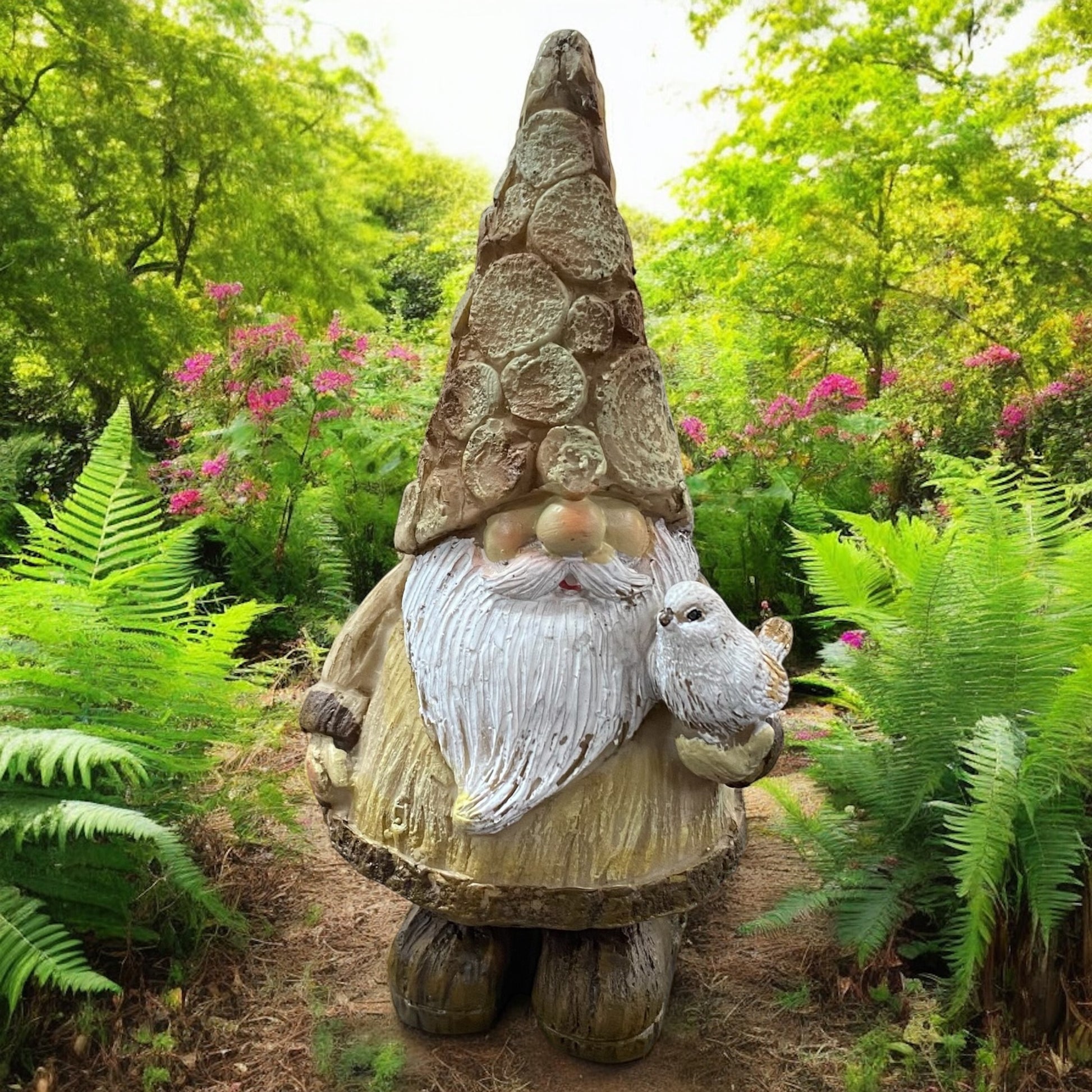 Goldener Wichtel mit langem Bart und Eule auf dem Arm, dekorativ im blühenden Garten platziert.