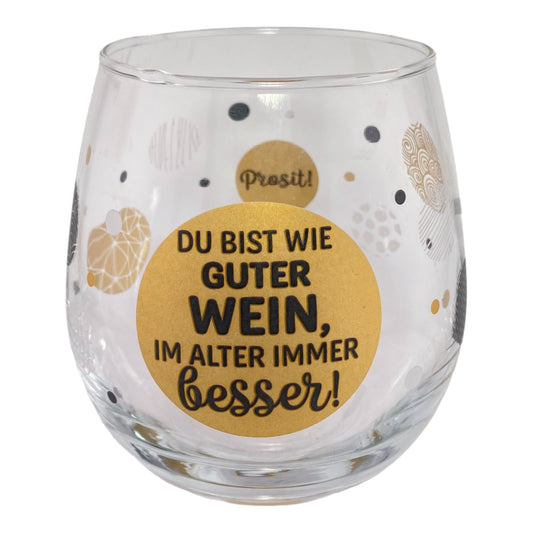 Glas mit Schriftzug "Du bist wie ein guter Wein, im Alter immer besser. Prost" vor weißem Hintergrund