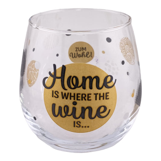 Glas mit Schriftzug "Home is where the wine is... zum Wohl" vor weißem Hintergrund