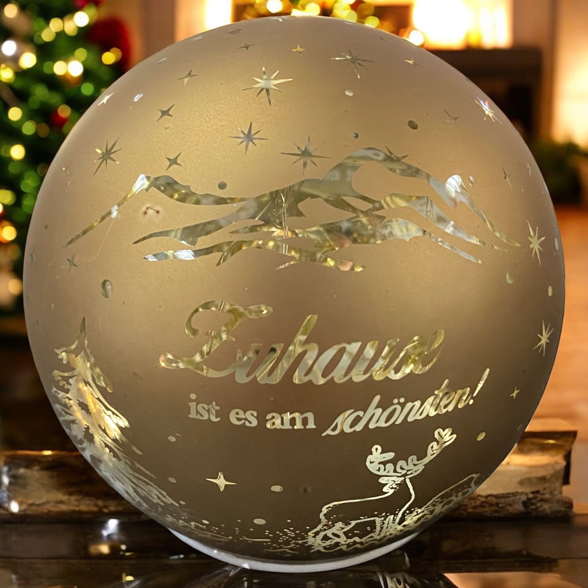 Dekorative goldene Lichtkugel mit Schriftzug „Zuhause ist es am schönsten“ und Rentiermotiv in festlicher Umgebung.