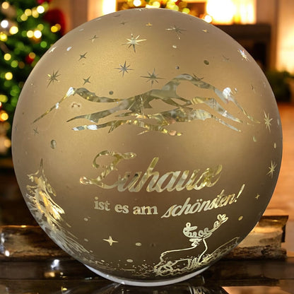 Dekorative goldene Lichtkugel mit Schriftzug „Zuhause ist es am schönsten“ und Rentiermotiv in festlicher Umgebung.