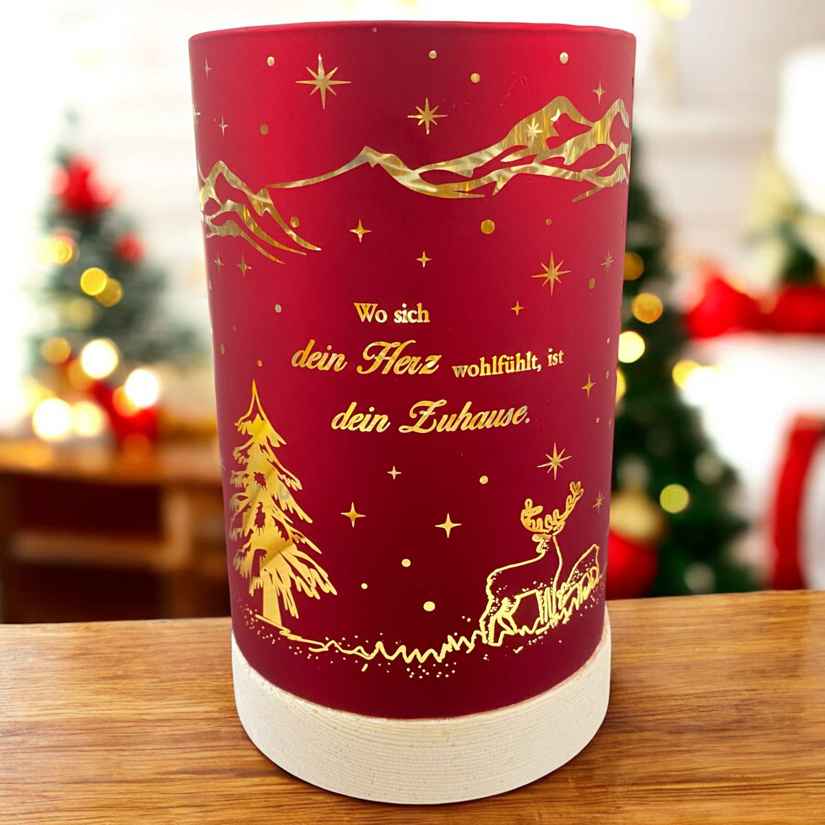 Kleines rotes Deko-Licht mit goldener Weihnachtslandschaft und dem Spruch „Wo sich dein Herz wohlfühlt, ist dein Zuhause“, auf Holztisch vor weihnachtlichem Hintergrund.