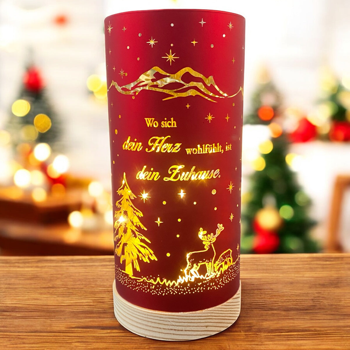 Großes rotes Deko-Licht mit goldenen Akzenten, beleuchtetem Hirschmotiv und dem Spruch „Wo sich dein Herz wohlfühlt, ist dein Zuhause“, vor weihnachtlich geschmücktem Raum.
