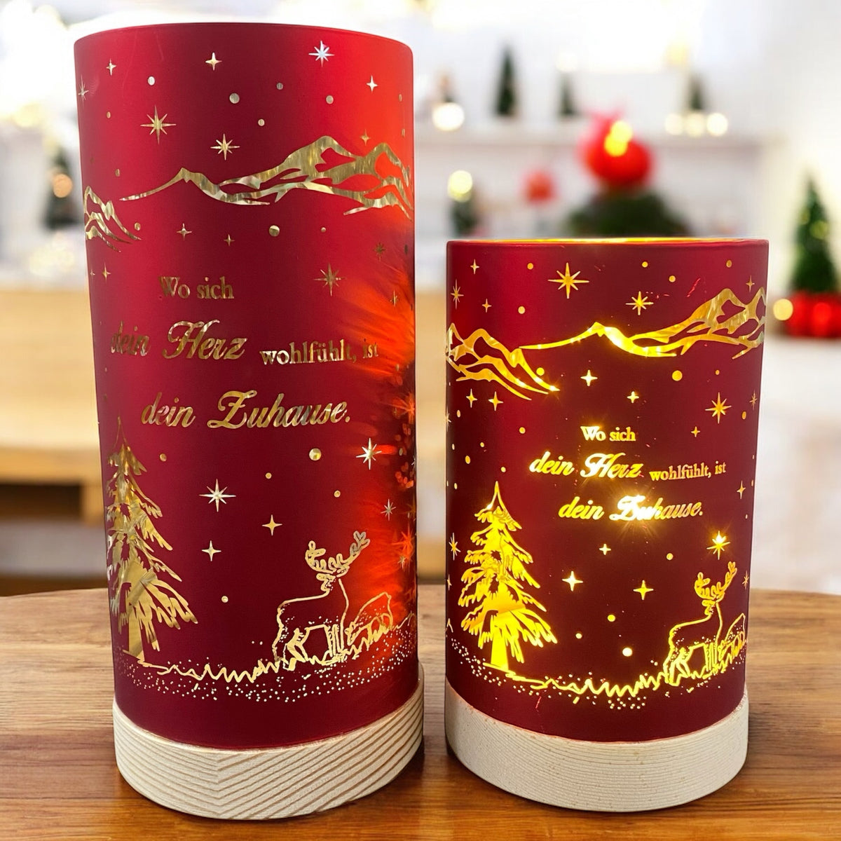 Zwei rote Deko-Lichter mit goldenen Motiven und dem Spruch „Wo sich dein Herz wohlfühlt, ist dein Zuhause“, mit Tannenbaum und Hirschmotiv im Ambiente