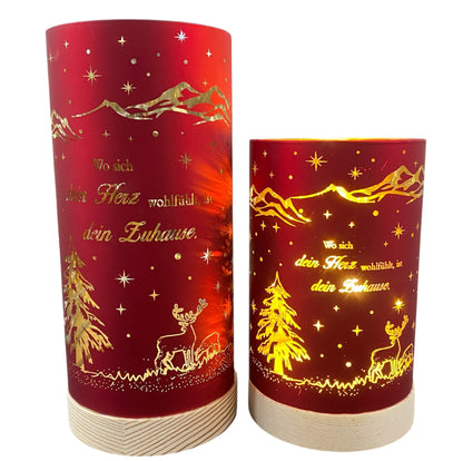 Zwei rote Deko-Lichter mit goldenen Motiven und dem Spruch „Wo sich dein Herz wohlfühlt, ist dein Zuhause“, mit Tannenbaum und Hirschmotiv