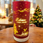 Großes rotes Deko-Licht mit goldener Aufschrift „Zuhause ist es am schönsten!“ und leuchtendem Hirschmotiv, auf Holztisch vor Weihnachtsbaum.

