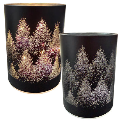 Zwei zylindrische schwarze Dekolichter mit perforiertem Tannenbaum-Motiv und hellem Innenlicht sind vor weißem Hintergrund dargestellt.