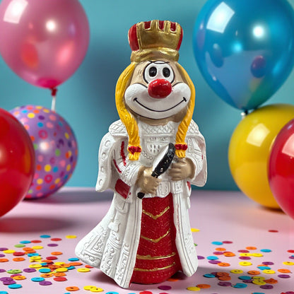 Clown-Figur in weiß-rotem Gewand mit Krone und Zopfdetails, hält ein schwarzes Objekt in den Händen, vor einem Hintergrund mit Luftballons und Konfetti.