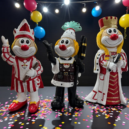 Drei Clown-Dekofiguren im Dreigestirn-Stil (Bauer, Jungfrau und Prinz), ca. 20 cm groß, auf einer Tischfläche mit Konfetti, im Hintergrund Luftballons und Lichter.