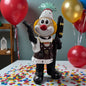 Clown-Dekofigur im Bauer-Kostüm, ca. 20 cm groß, mit erhobener Hand, stehend auf einer Tischfläche mit Konfetti, im Hintergrund farbige Luftballons.