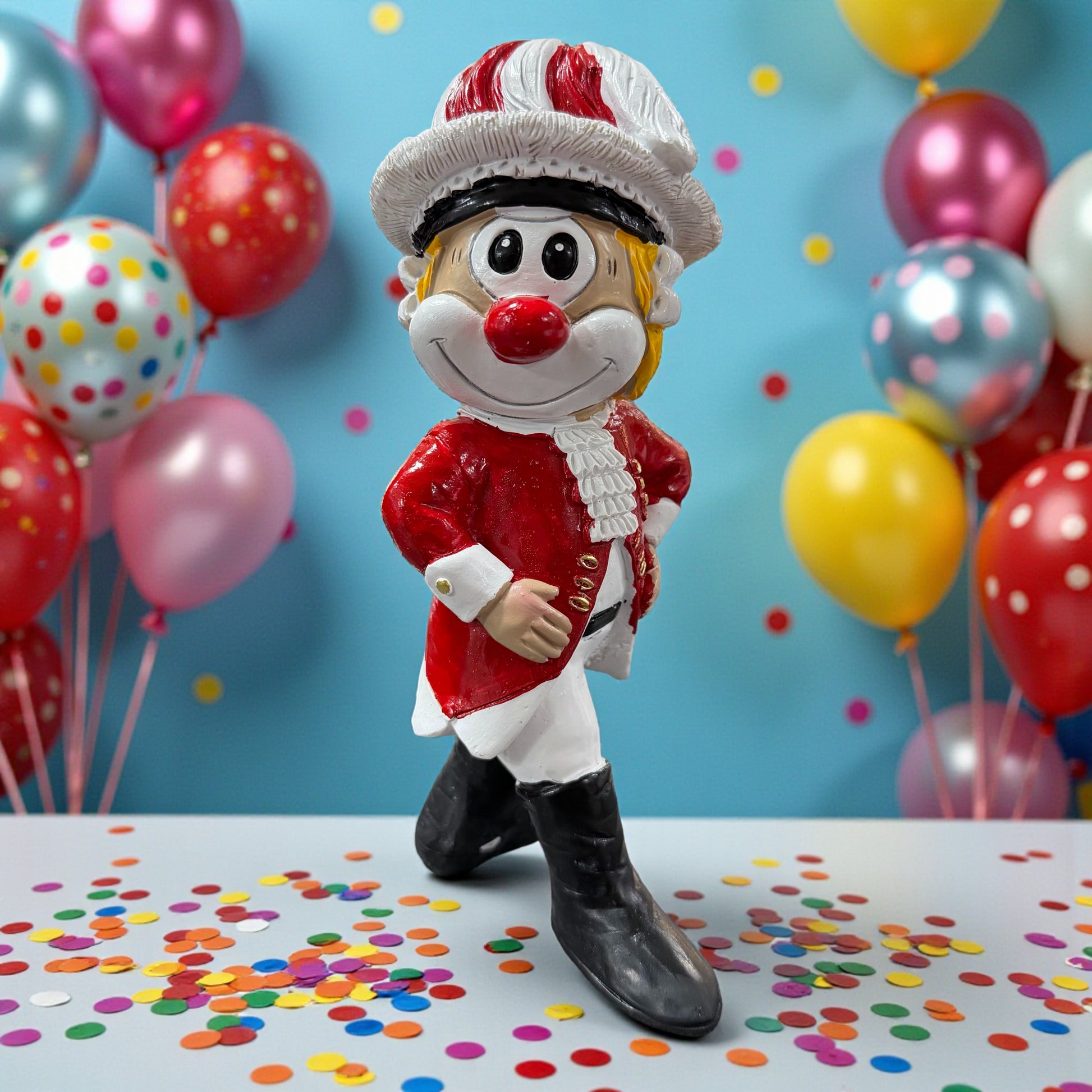 Große Clown-Dekofigur mit roter Nase im rot-weißen Tanzmajor-Outfit, ca. 20 cm groß, mit einer Hand in die Hüfte gestützt, auf einer Tischfläche mit Konfetti, im Hintergrund bunte Luftballons.