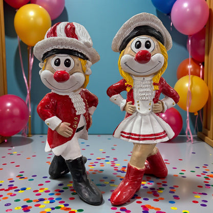 Zwei große Clown-Dekofiguren mit roter Nase im Tanzmajor- und Tanzmarie-Outfit, ca. 20 cm groß, auf einer Tischfläche mit Konfetti, im Hintergrund bunte Luftballons.