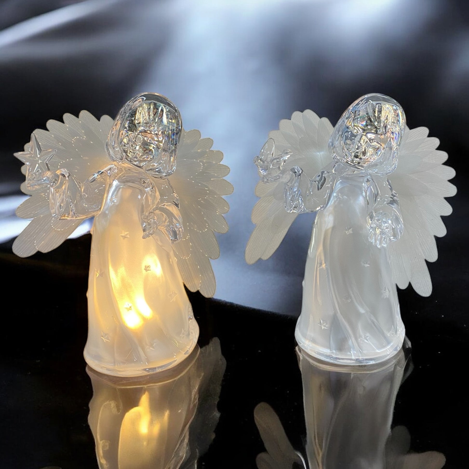 Zwei transparente Acryl-Engelfiguren mit Flügeln, eine Figur leuchtet warm von innen, die andere ist unbeleuchtet im Ambiente