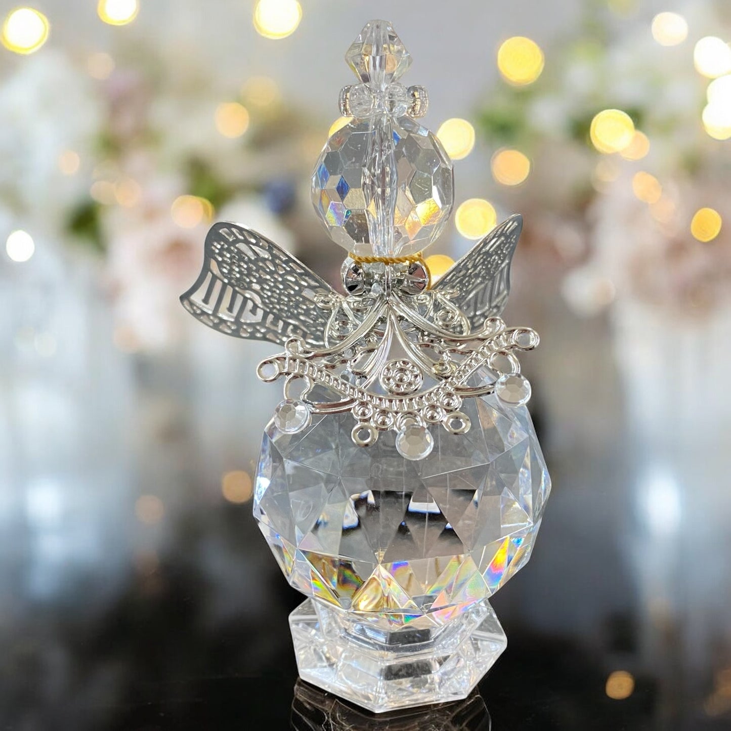 Eine gläserne Deko-Engelfigur mit facettiertem Körper und silberfarbenen Flügeln sowie filigranen Verzierungen in unterschiedlichen Größen im Ambiente