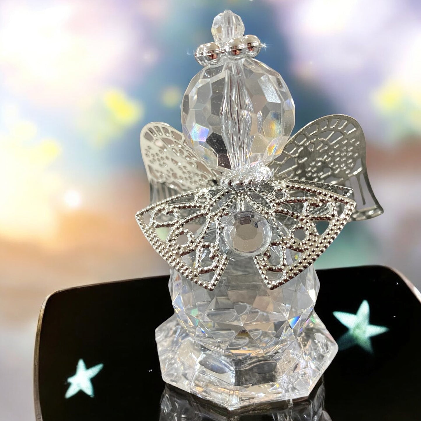 Eine kleine gläserne Deko-Engelfigur mit facettiertem Körper und silberfarbenen Flügeln sowie filigranen Verzierungen in unterschiedlichen Größen im Ambiente